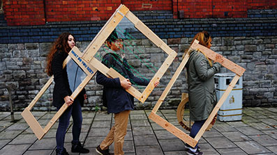 Three students carrying display frames down the street Three students carrying display frames down the street