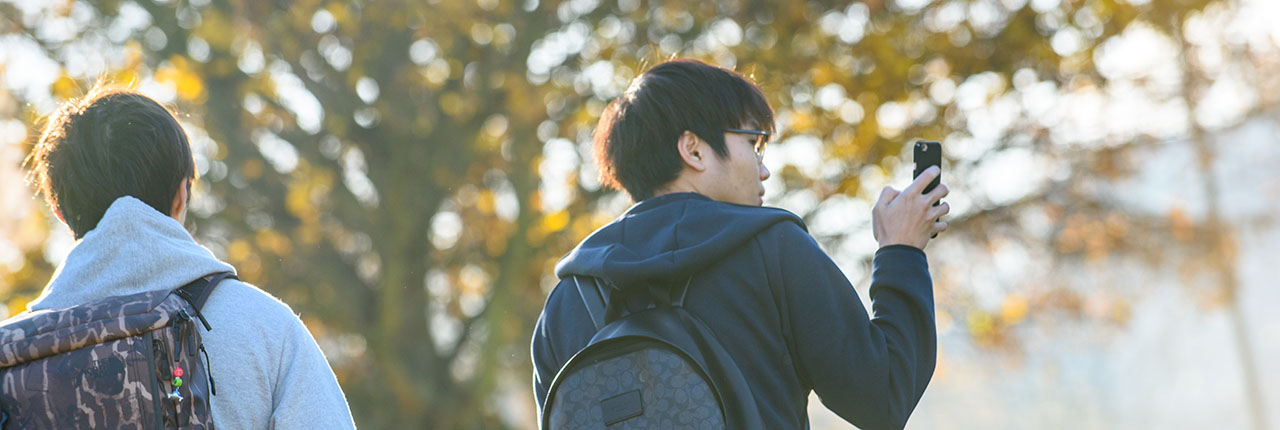 Two people walking as light shines through autumn leaves on the trees