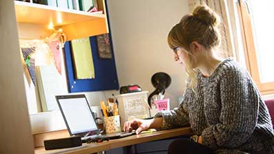 Female student using her laptop in a bedroom Female student using her laptop in a bedroom
