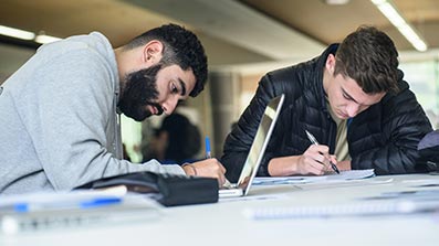 Two students studying with pen, paper and a laptop Two students studying with pen, paper and a laptop